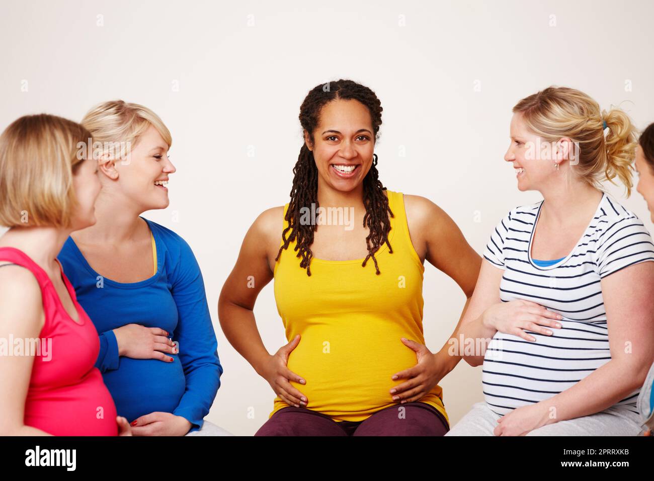 Sharing their experiences. A multi-ethnic group of pregnant women sitting together and having a friendly discussion while one smiles at the camera. Stock Photo