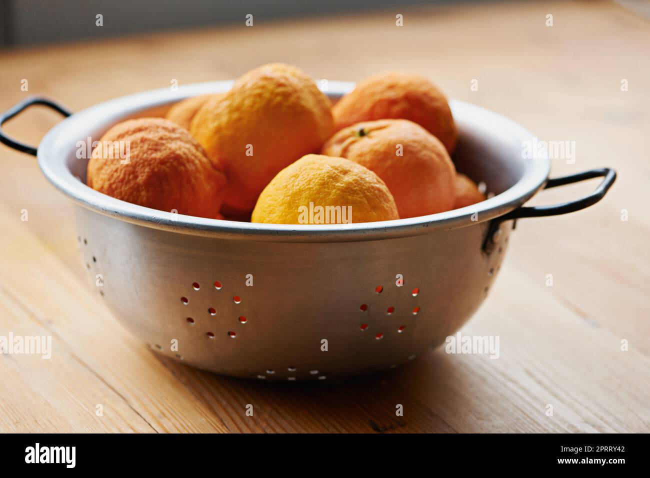 Citrus snacking. a colander full of tangerines on a kitchen table. Stock Photo