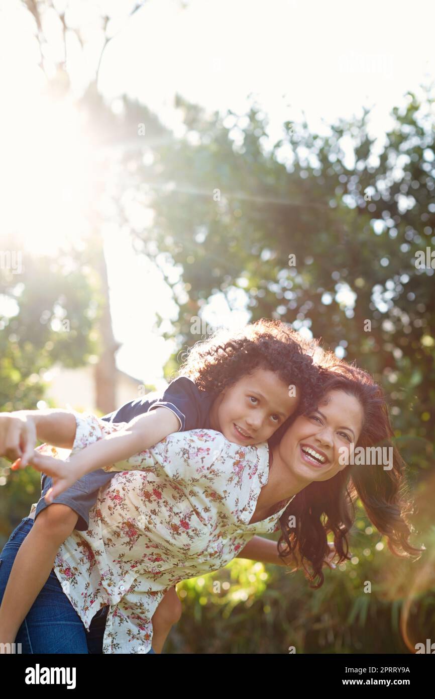 Hes my greatest joy. A young mother piggybacking her son in the park. Stock Photo