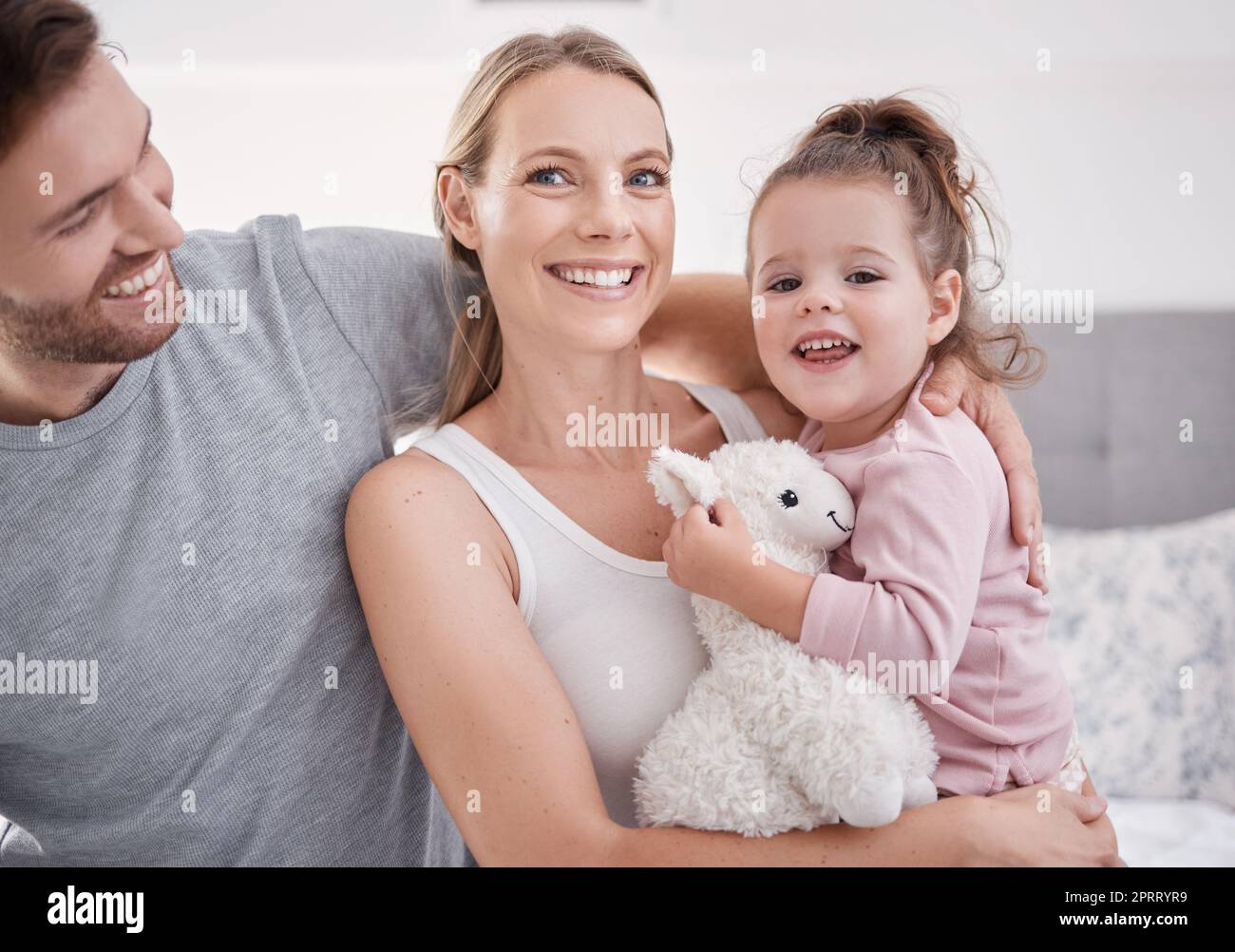 Family, love and children with a mother, father and girl sitting on a bed in their home together during the morning. Kids, parents and happy with a woman, man and their daughter relaxing in a bedroom Stock Photo