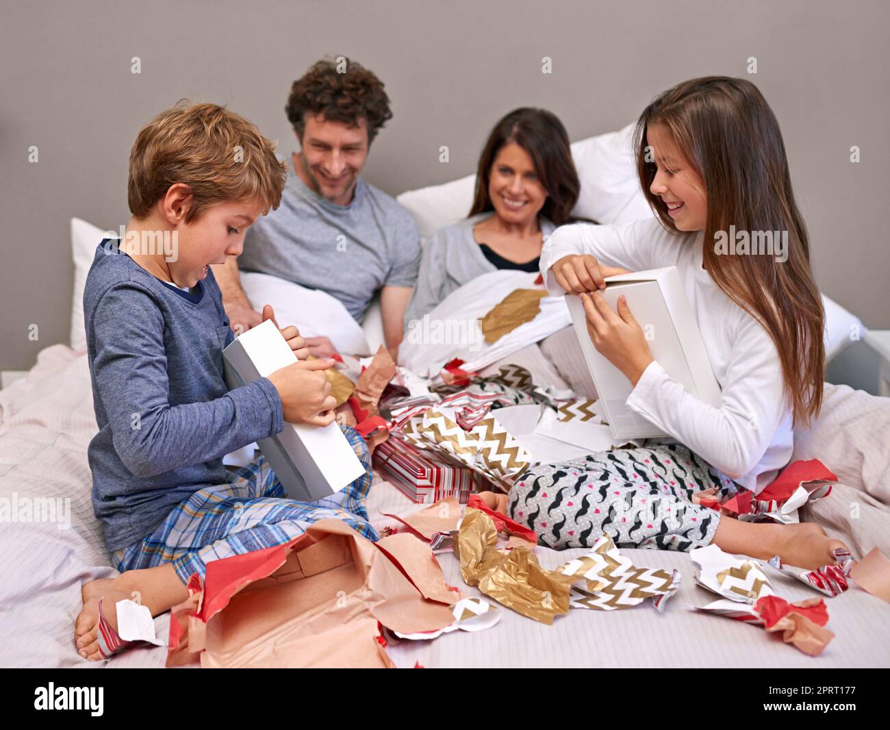 We couldnt wait any longer. two children opening presents on their parents bed in the morning. Stock Photo