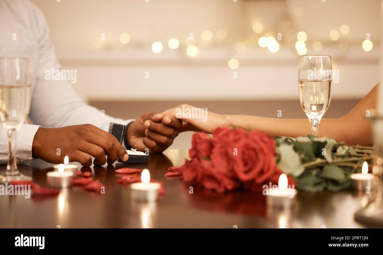 Love, engagement and couple holding hands with wedding ring at restaurant table for proposal, date and celebration. Romance, champagne and happiness with diamond jewellery for marriage Stock Photo