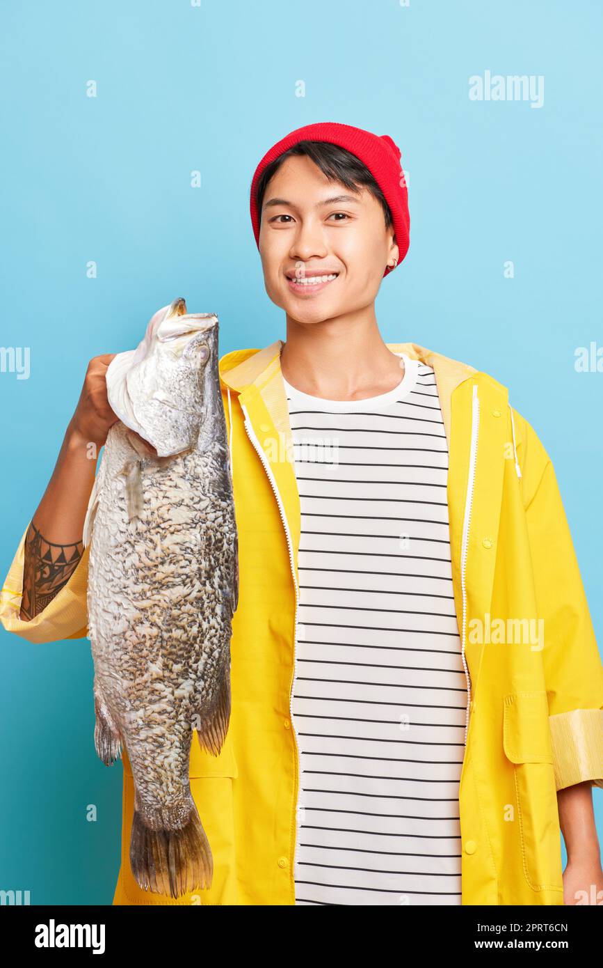 Smiling young fisherman holds big fish in his hand, wearing red cap
