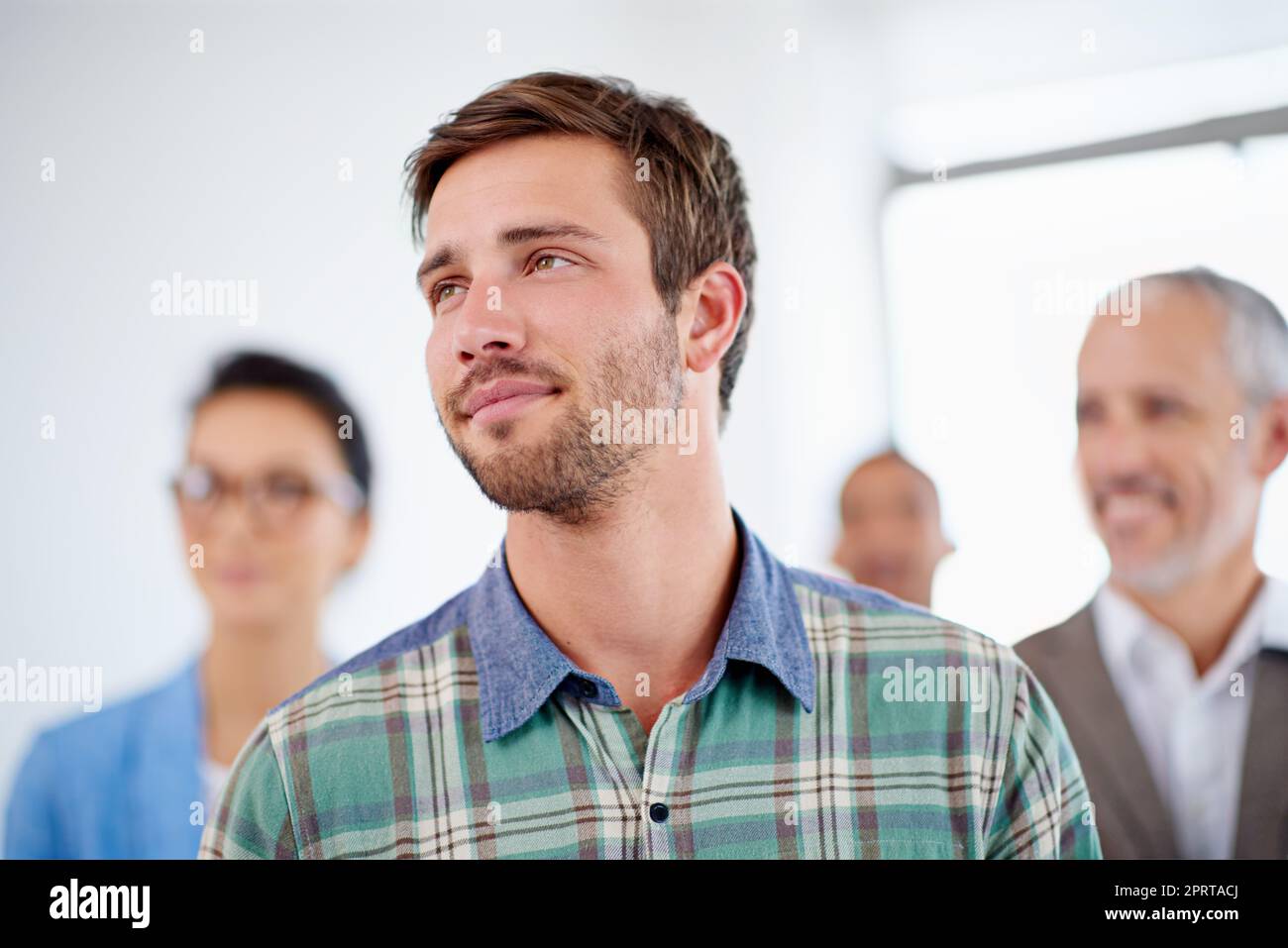 The futures looking promising. Young man looking away with coworkers in the background. Stock Photo