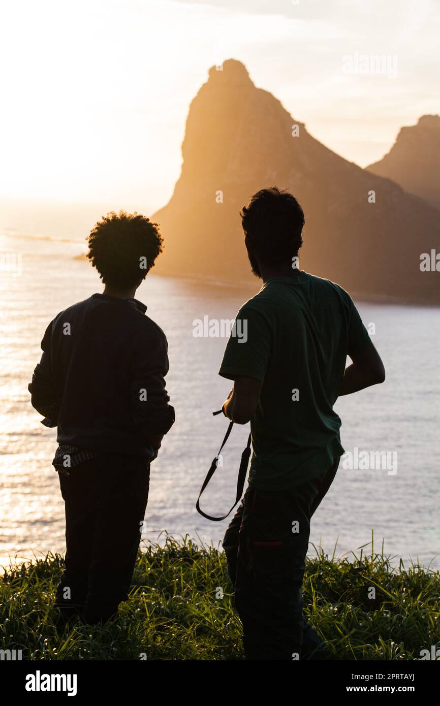 Taking in natures magnificence. Rearview shot of two men enjoying an ocean view from a hilltop. Stock Photo