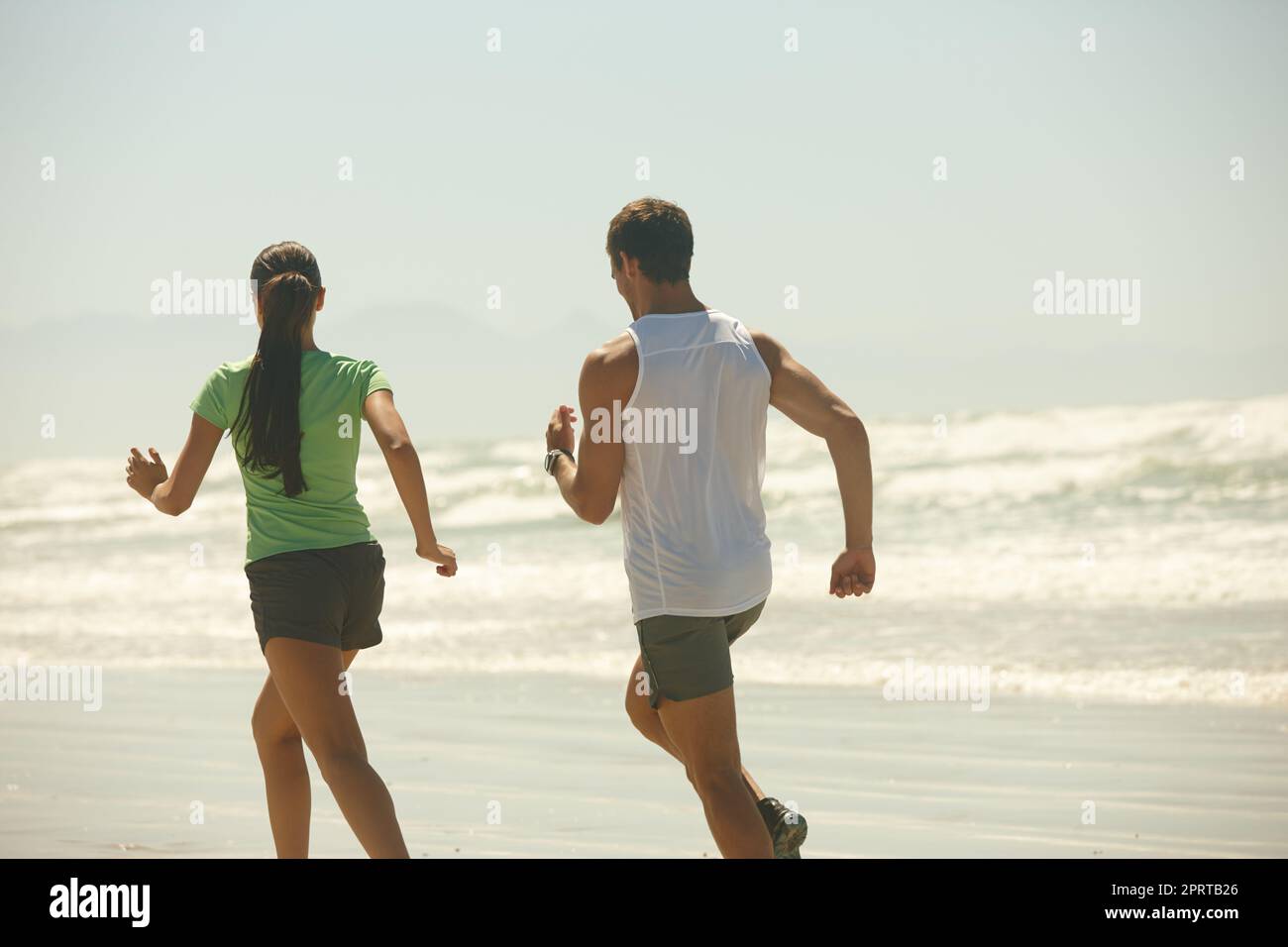 Its funny how things work out sometimes. Rearview shot of a couple jogging along the beach. Stock Photo