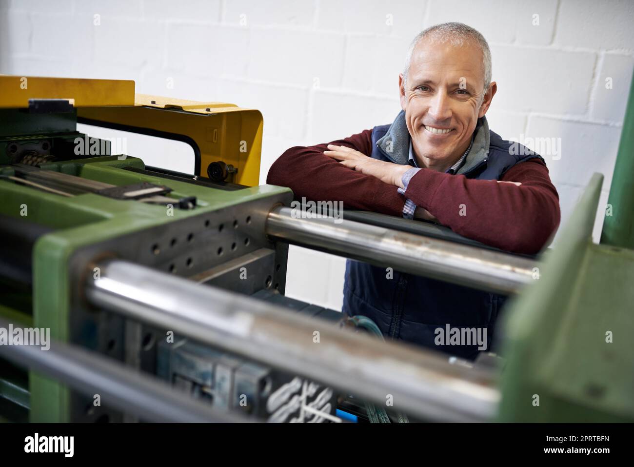 If you need something fixed, Im your man. Portrait of a mature man standing next to machinery in a factory. Stock Photo