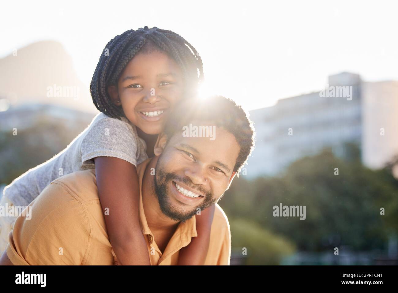 Happy black father carrying girl, child or kid outdoors in nature park outside. Portrait, support and love of caring male parent bonding with daughter with a smile together while taking a walk. Stock Photo