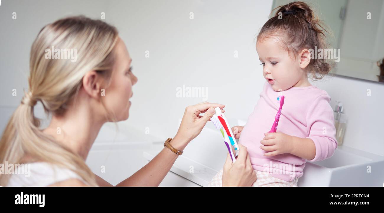 Baby kid brushing teeth with mom in bathroom, morning oral hygiene and clean dental healthcare wellness. Parent with toothpaste and toothbrush teaching young toddler girl child healthy mouth cleaning Stock Photo
