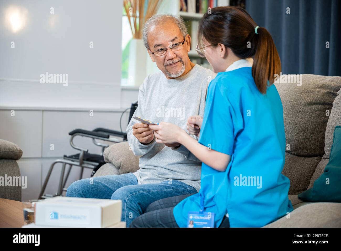 Asian nurse with physician explaining prescription medicine to attentive senior man at home Stock Photo
