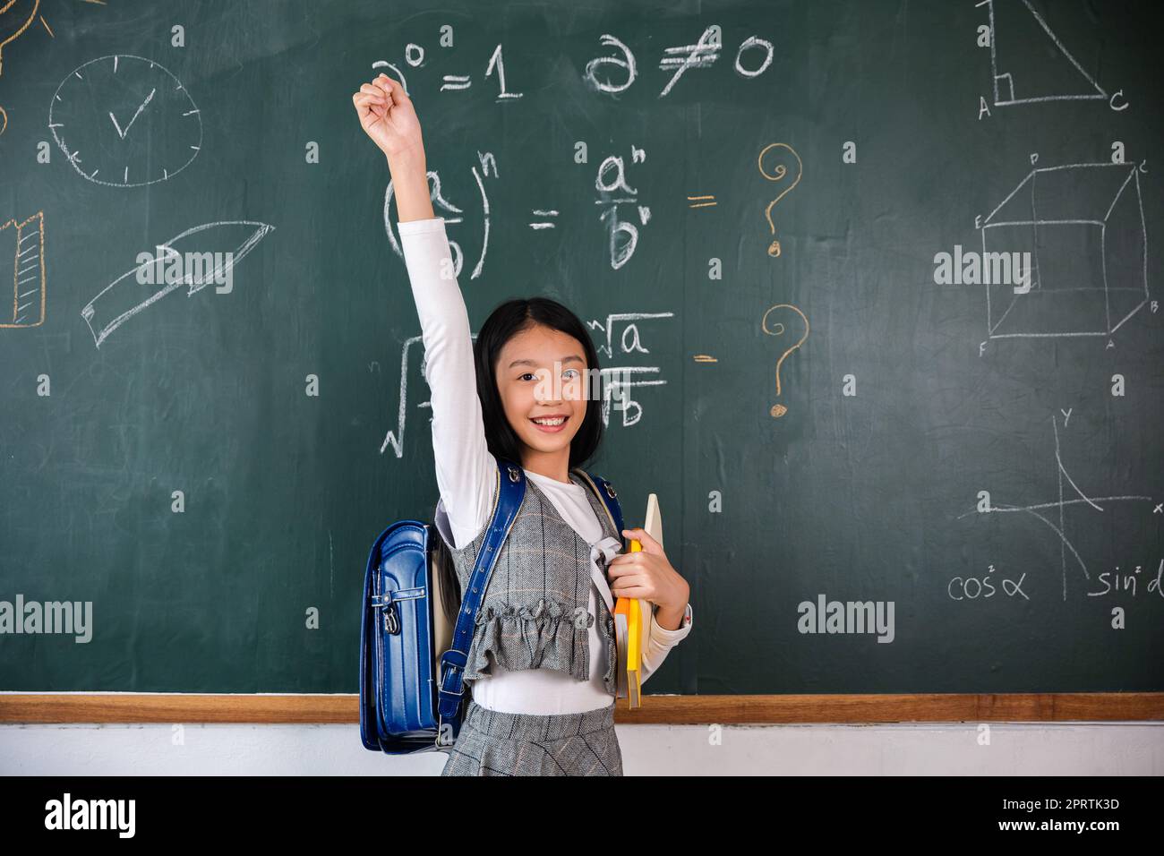 Asian school girl in uniform on classroom raised arms to successful finished homework Stock Photo