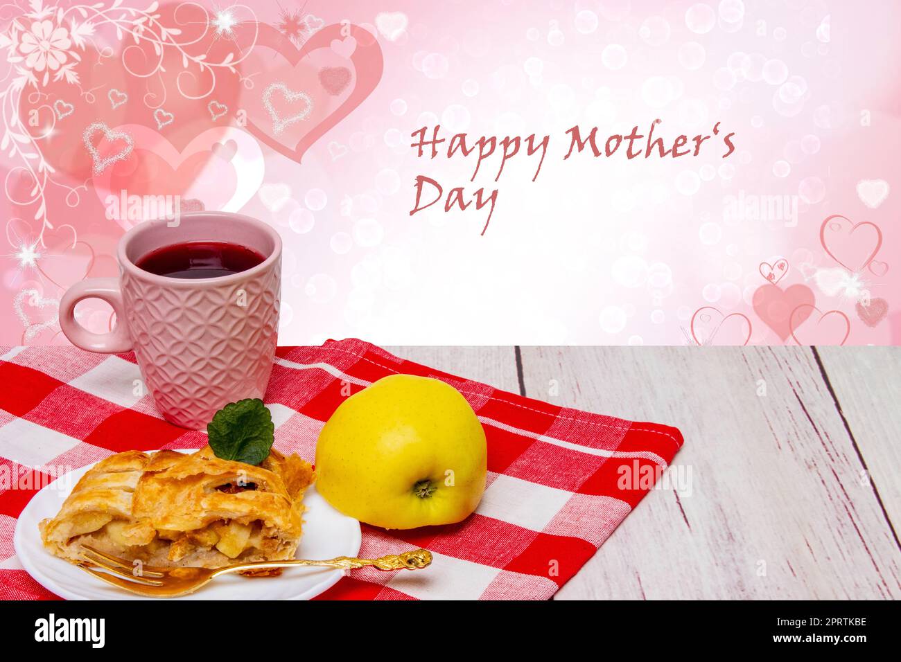 A slice of homemade baked fresh apple strudel with a cup of coffee and a fresh apple on red picnic cloth over abstract hearts bokeh background. Happy Mothers Day text. Stock Photo