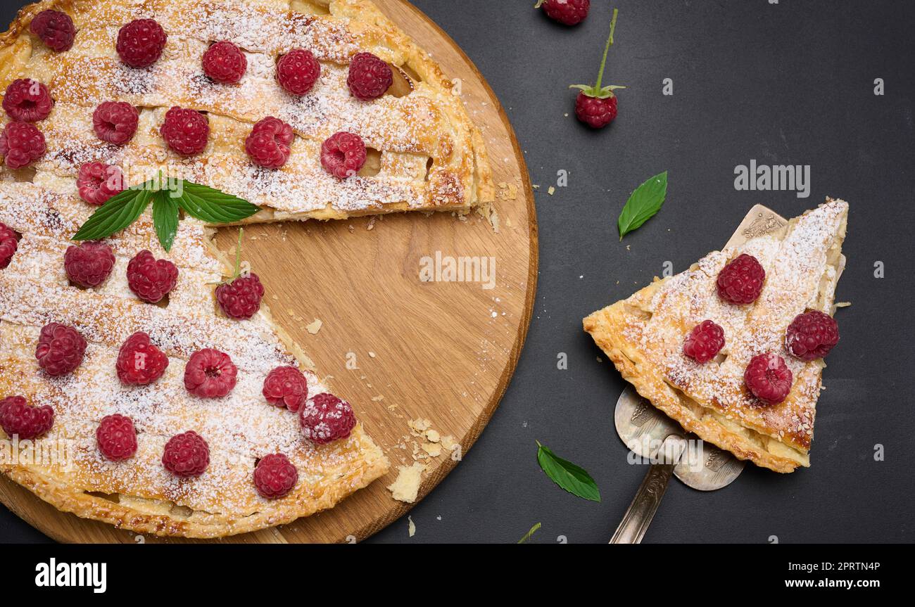 Round baked pie with apples and sprinkled with powdered sugar on a black table. Stock Photo