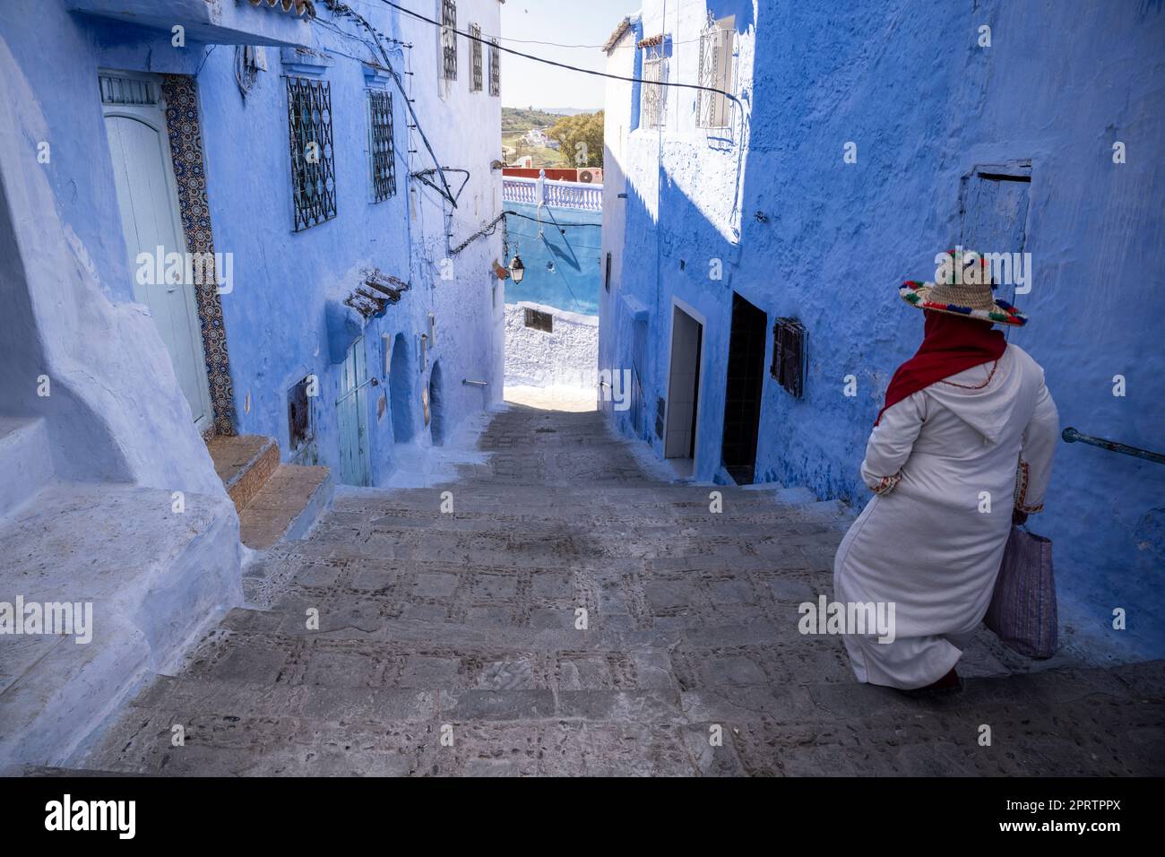 Woman going down the stairs of a steep alley in the medina of Chefchaouen. Stock Photo