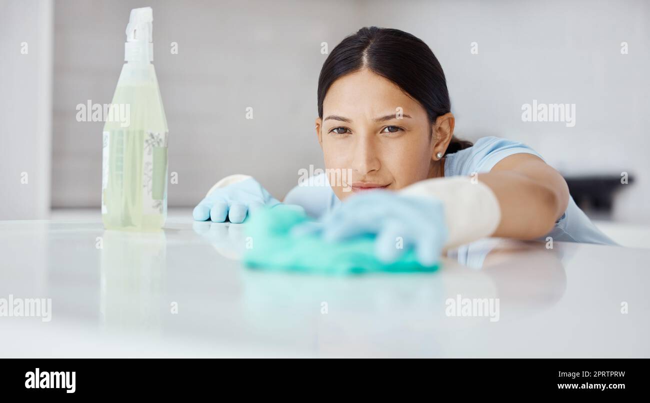 Kitchen, product and cleaner cleaning a table with dirt or dust with detergent, cloth and gloves. Woman maid, domestic employee or housewife doing housekeeping in a modern office or house. Stock Photo
