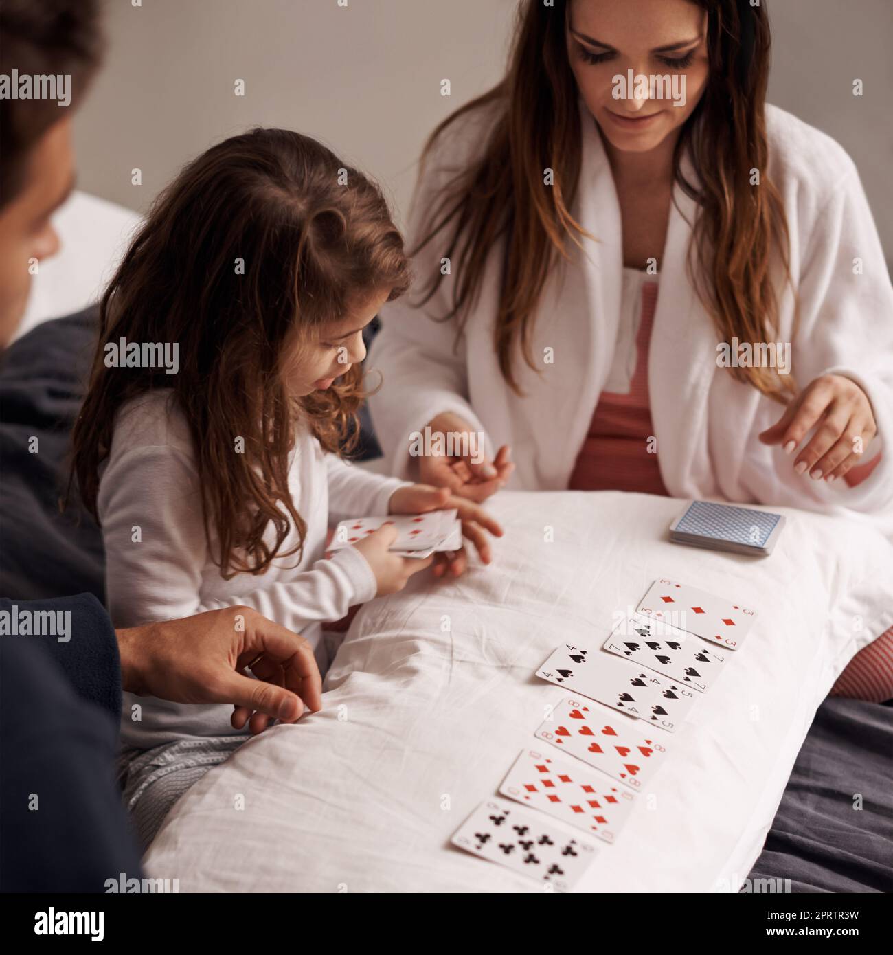 Contemplating her next move. a young family playing cards together at home. Stock Photo