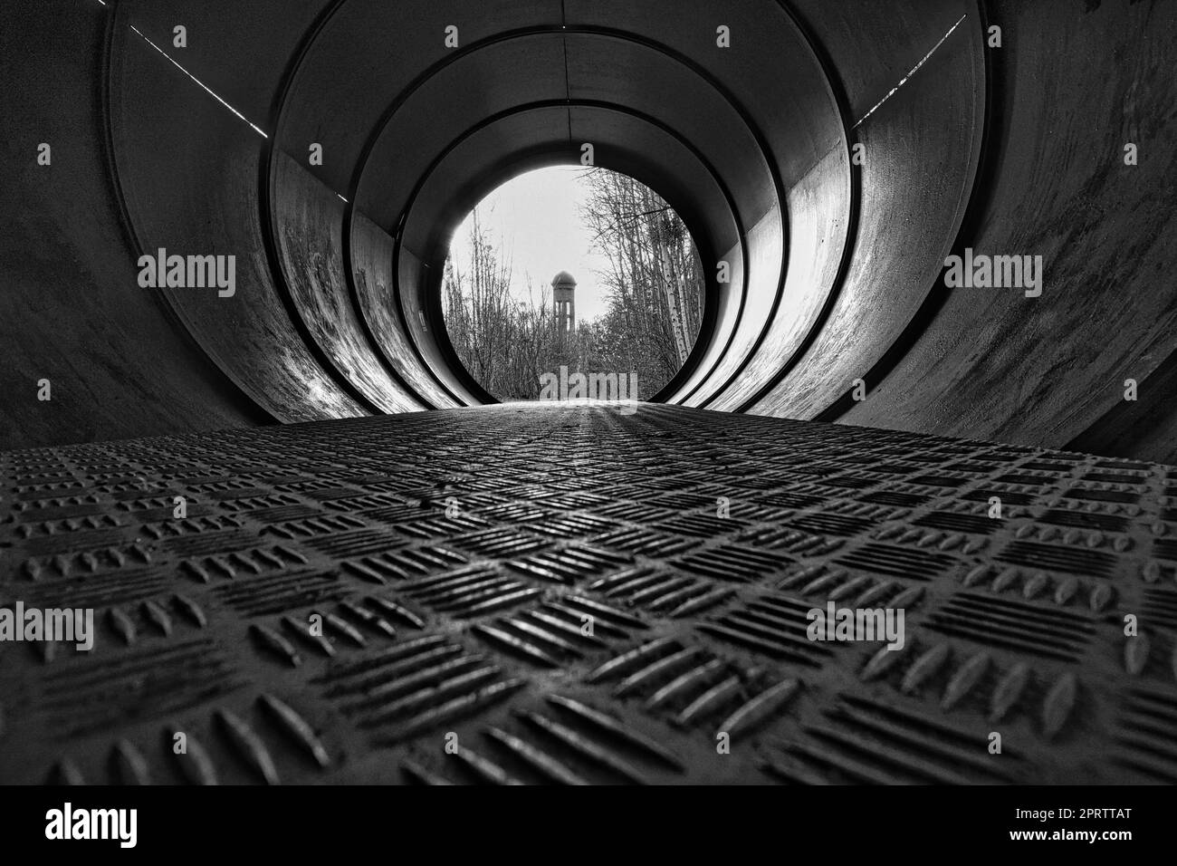 View through a metal pipe. In the background between trees is a water tower. Stock Photo