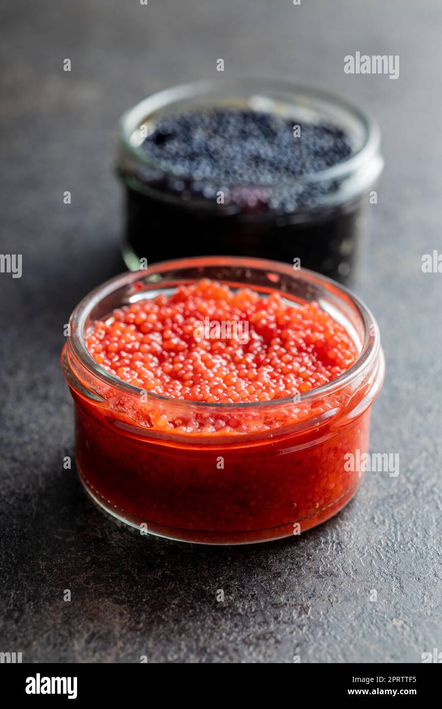 Red and black caviar in jar on dark table. Stock Photo