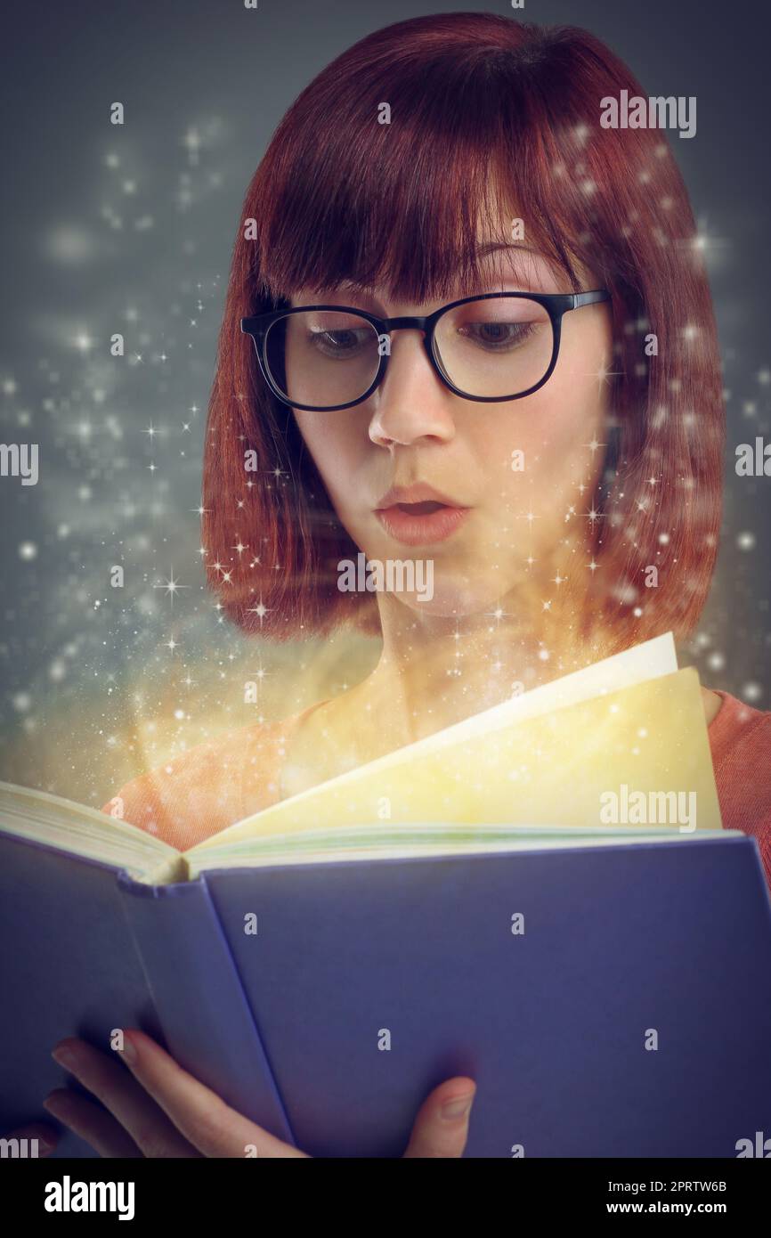 Drawn deeper into the magic of the story. A cropped shot of a young adult reading a book with glowing pages. Stock Photo