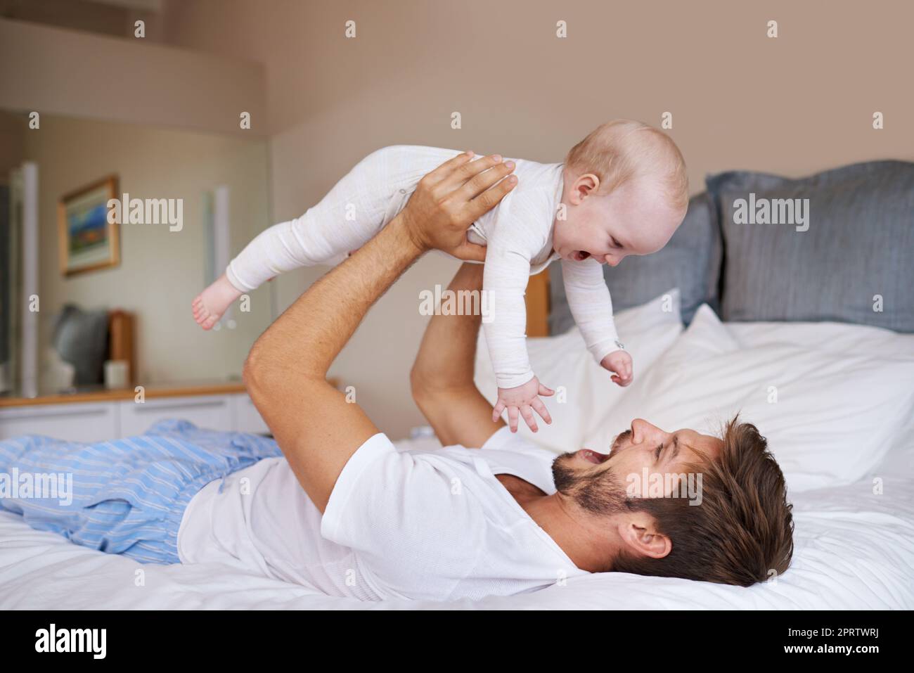 I could just eat you up. a father lying on a bed holding his baby girl up in the air. Stock Photo