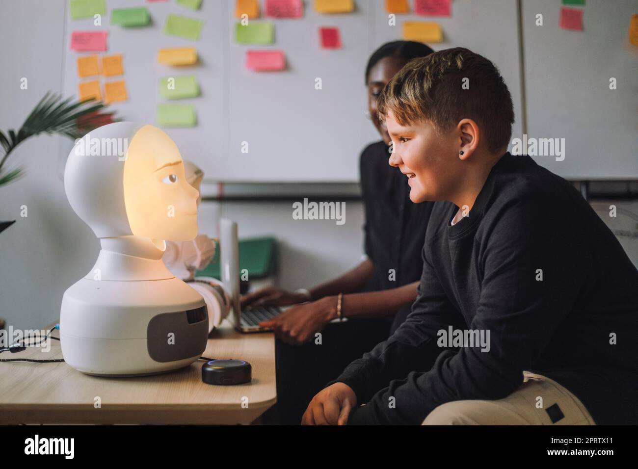 Smiling boy communicating with illuminated AI robot in innovation lab Stock Photo