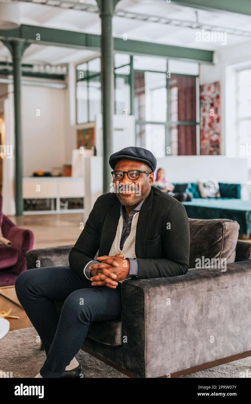 Smiling businessman looking away while sitting on sofa at office Stock Photo
