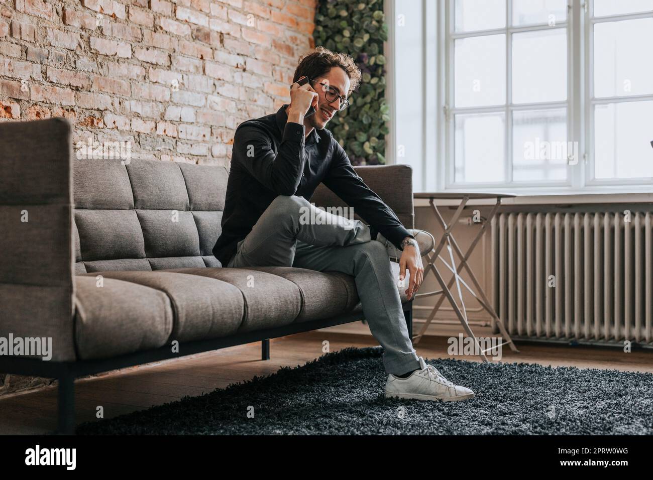Smiling businessman talking on smart phone while sitting on sofa at office Stock Photo
