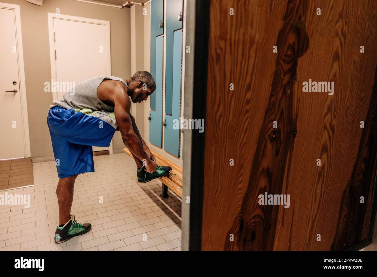 Side view of male athlete tying shoe lace in locker room Stock Photo