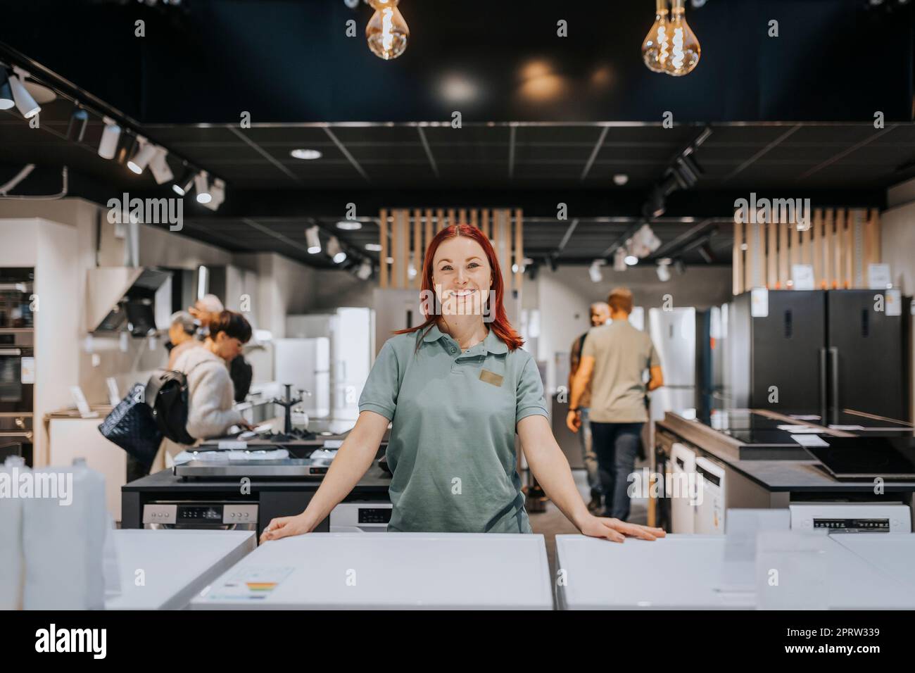 Portrait of smiling female sales clerk leaning on washing machine in electronics store Stock Photo