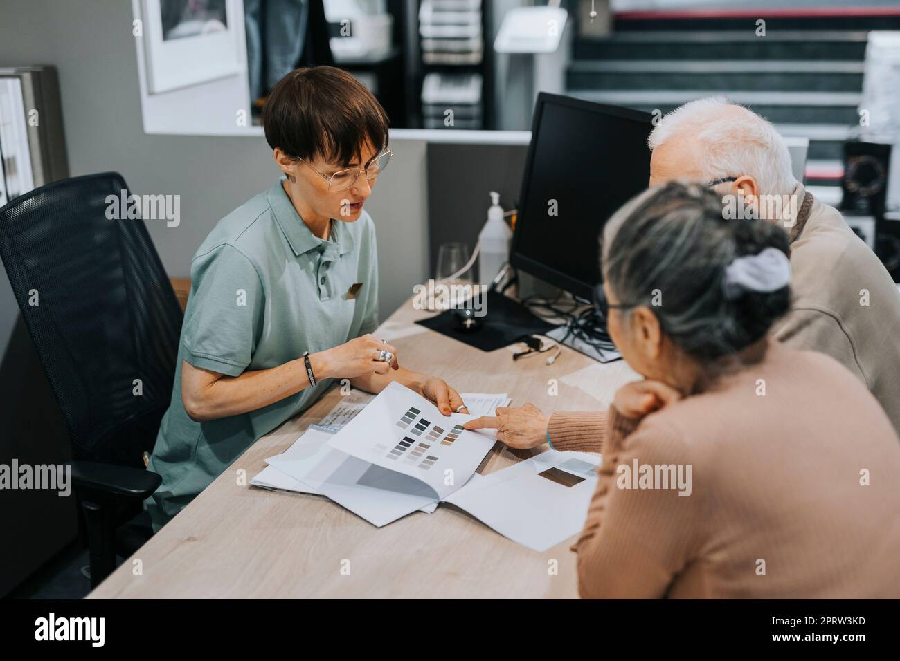 Senior couple discussing with female interior designer over brochure at desk in store Stock Photo