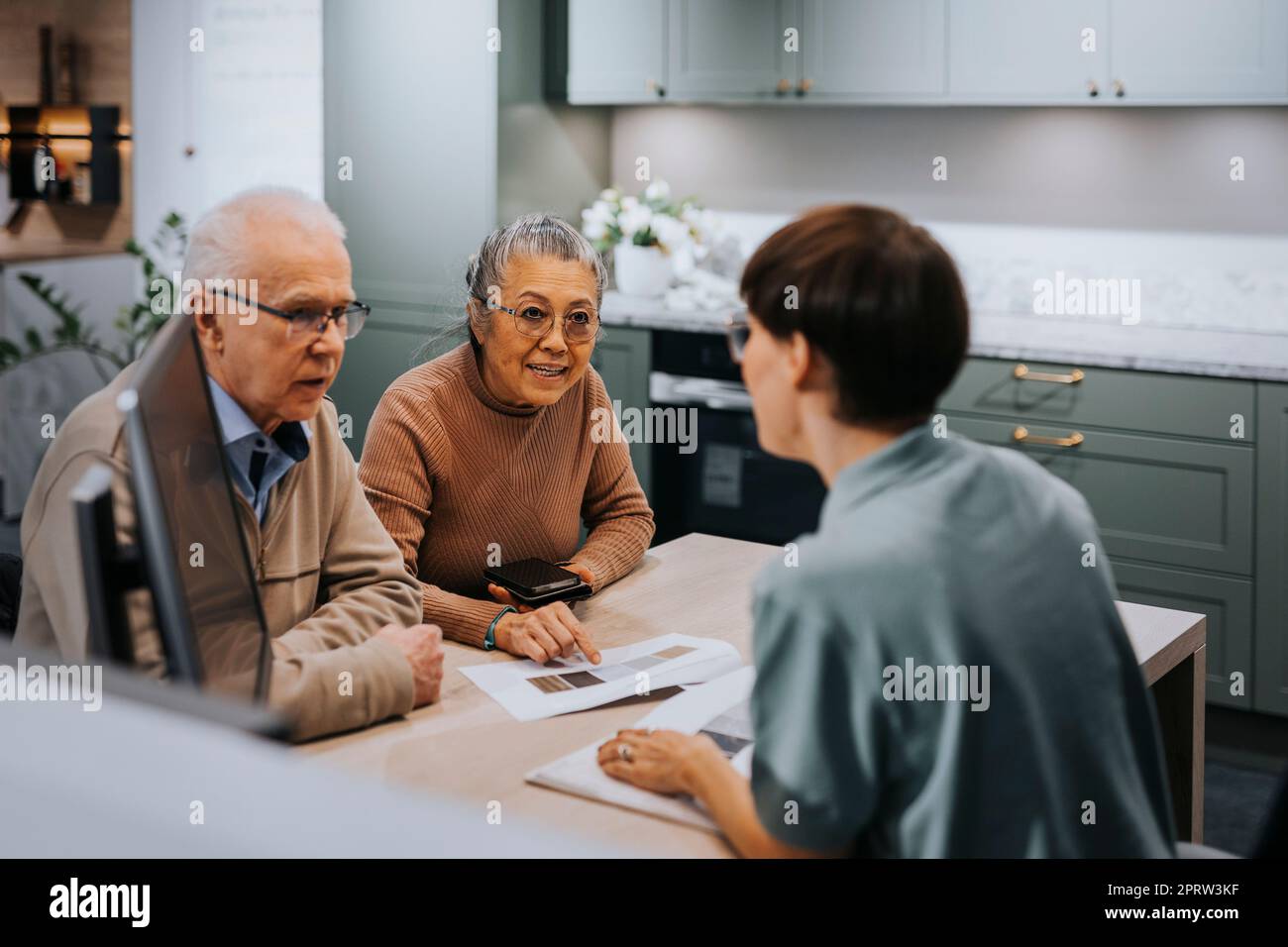 Senior couple discussing with interior designer over brochure while sitting at desk in store Stock Photo