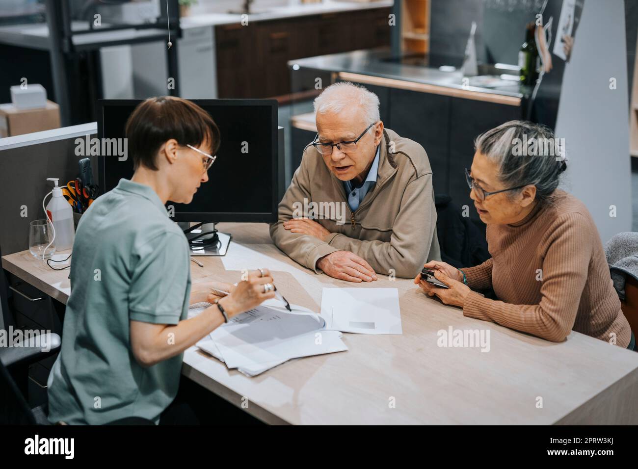 Female interior designer discussing over brochure with senior couple at desk in store Stock Photo