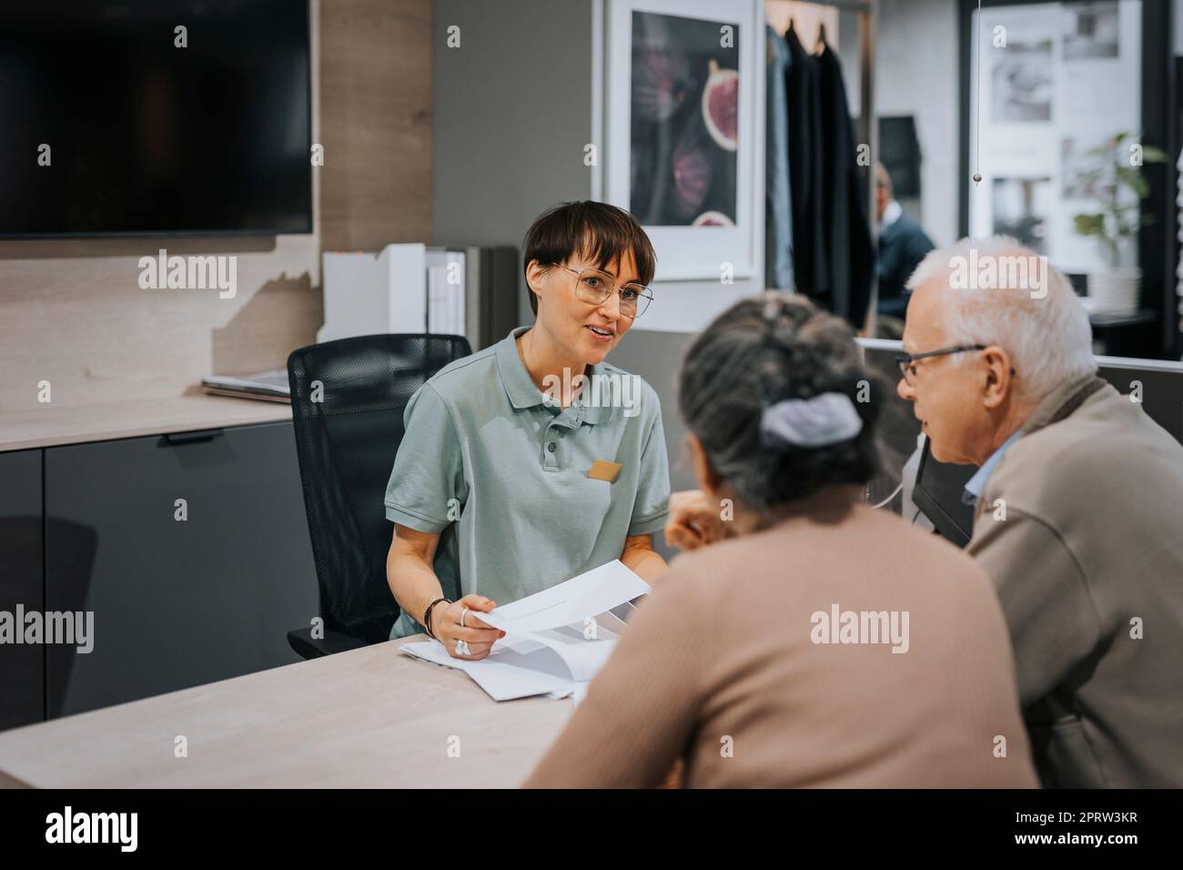 Smiling female interior designer explaining senior couple over brochure at desk in store Stock Photo