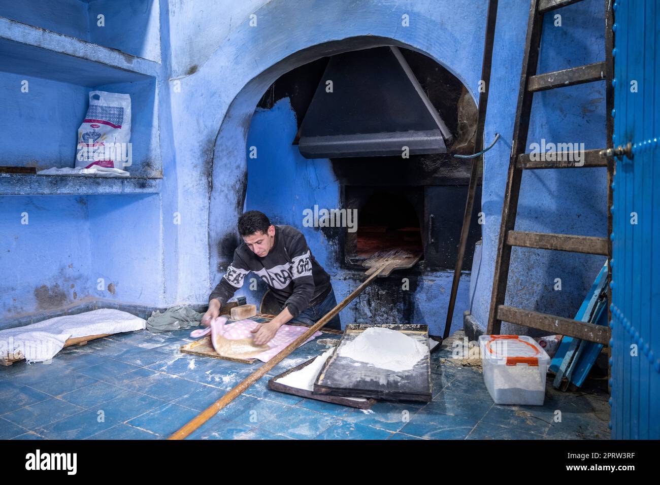 Baker baking bread in a traditional wood-fired oven in the medina of Chefchaouen. Stock Photo