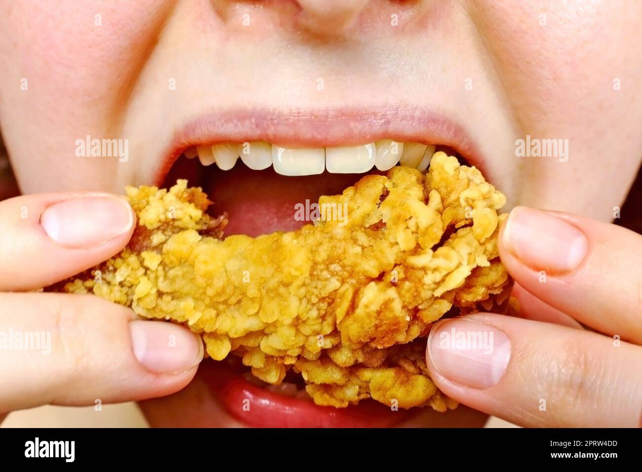 Woman eating a takeaway fried chicken wing from fast food cafe with a mouth and teeth close up. Stock Photo