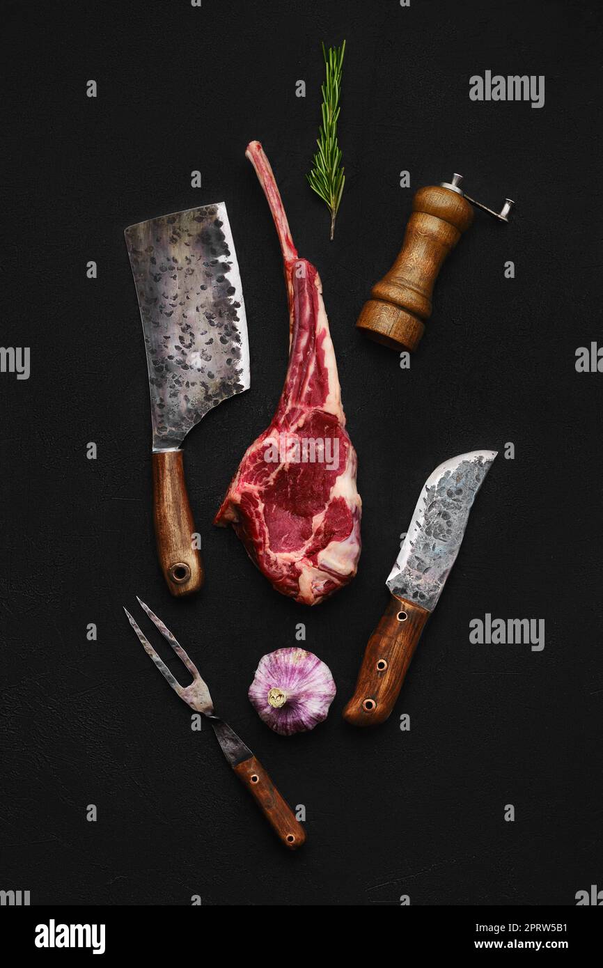 Overhead composition with raw beef cowboy steak and butcher tools on