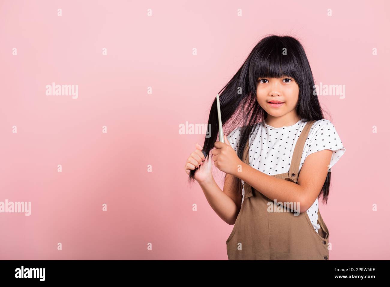 Asian little kid 10 years old hold comb brushing her unruly she touching her long black hair Stock Photo