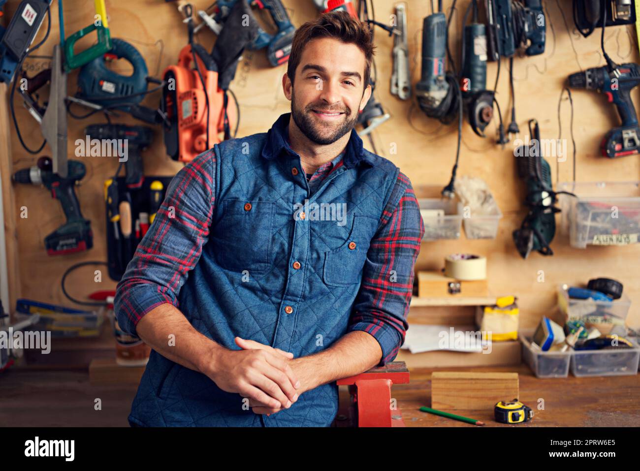 If its broken Ill fix it. Portrait of a handsome young handyman standing in front of his work tools. Stock Photo