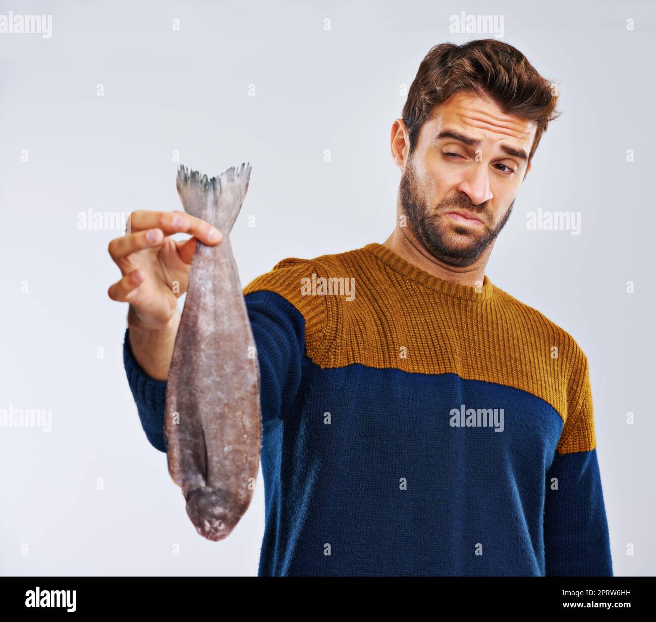 Theres something fishy going on here. Studio shot of a man showing disgust while holding a smelly fish. Stock Photo