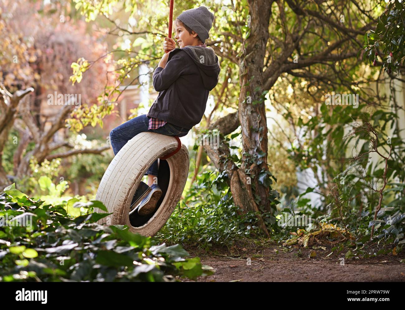 Carefree summer days of an idyllic childhood. A preteen boy swinging on a tyre swing in the garden. Stock Photo