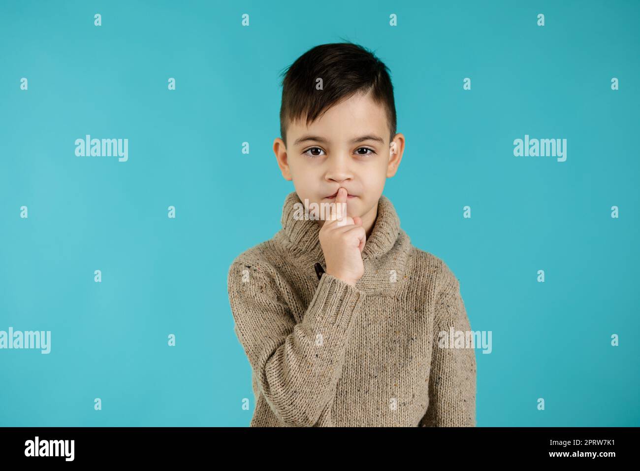 cute little boy asking to be quiet with finger on lips on blue