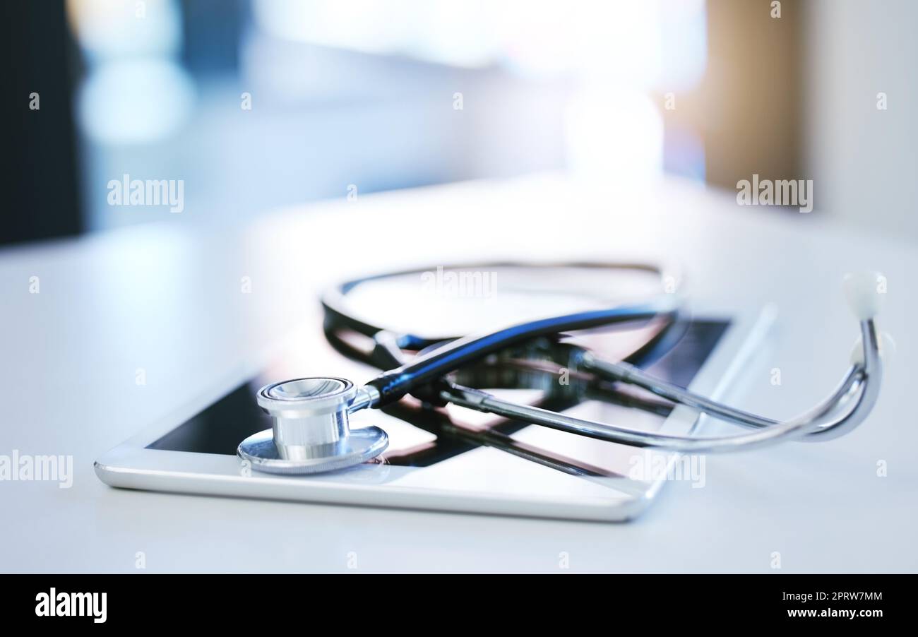 Digital tablet, stethoscope and telehealth consulting on table in empty hospital, wellness and medicine insurance room. Zoom on medical equipment, healthcare research and internet technology for help Stock Photo