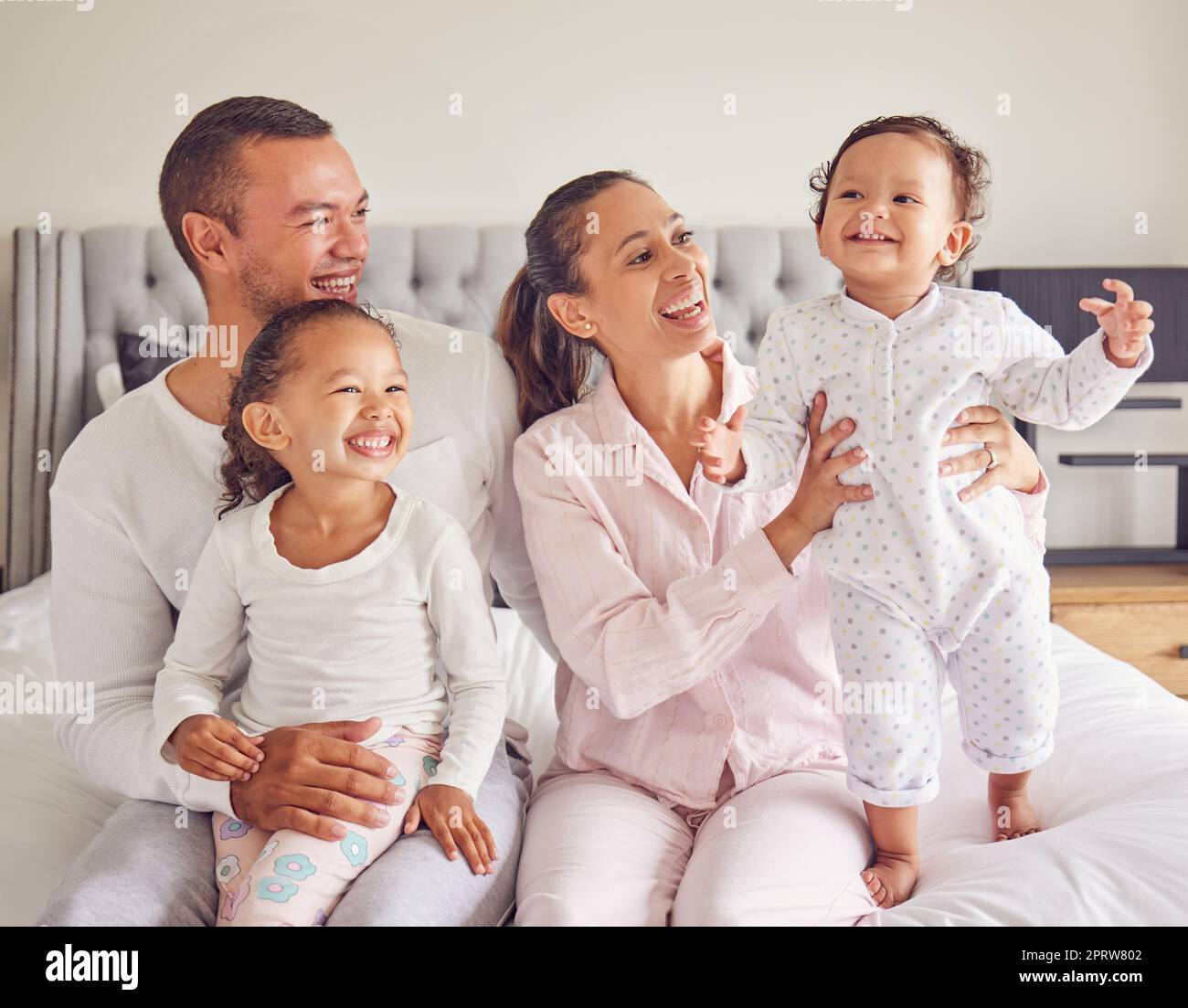 Happy family, love and morning bonding with parents, child and baby playing in the bedroom and having fun together at home. Loving man and woman spending time with their playful kids to relax Stock Photo