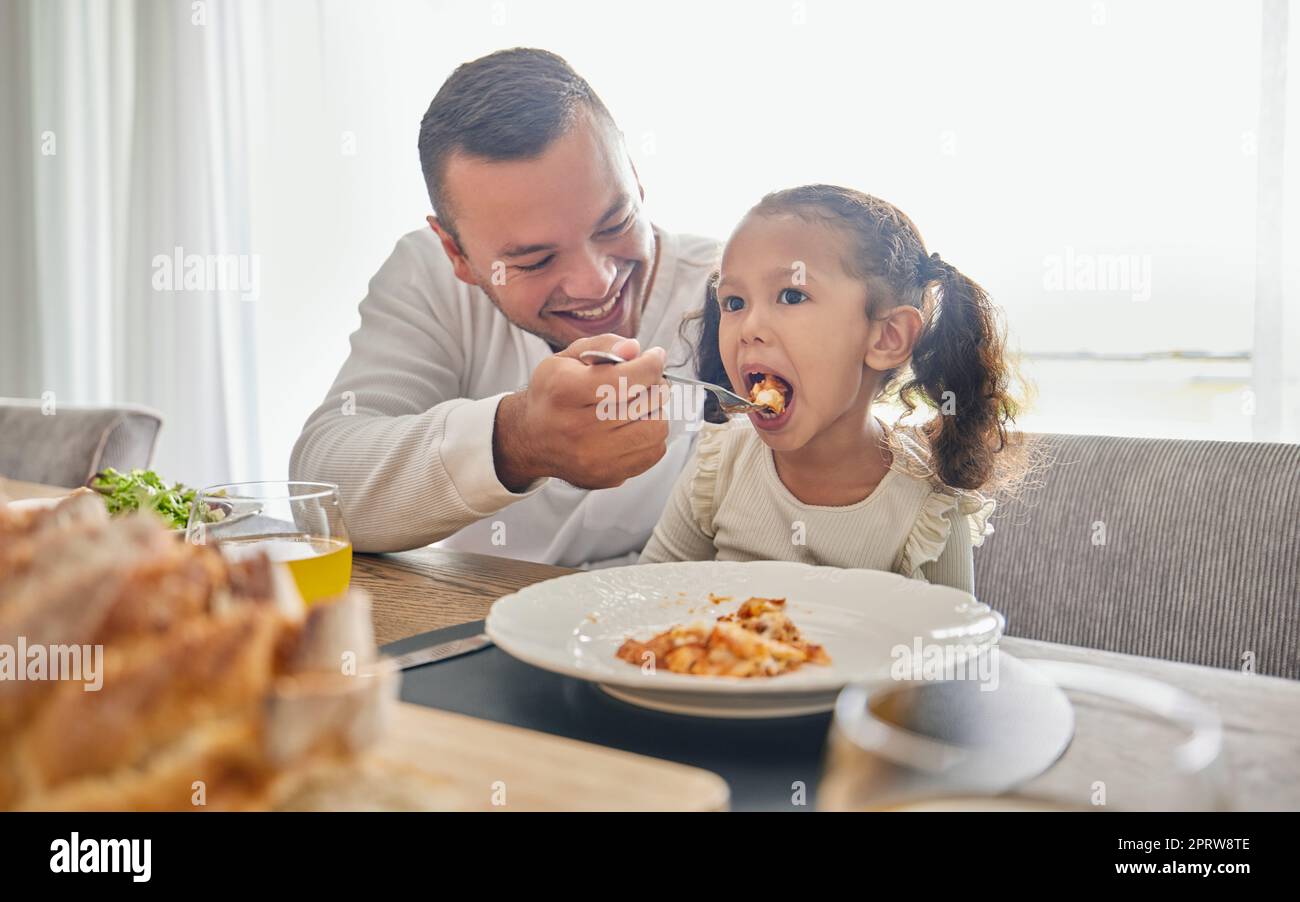 Father feed lunch food to girl for support with health, child development and growth while relax at home. Eating meal, dad or man feeding kid daughter while happy and enjoy quality time together Stock Photo