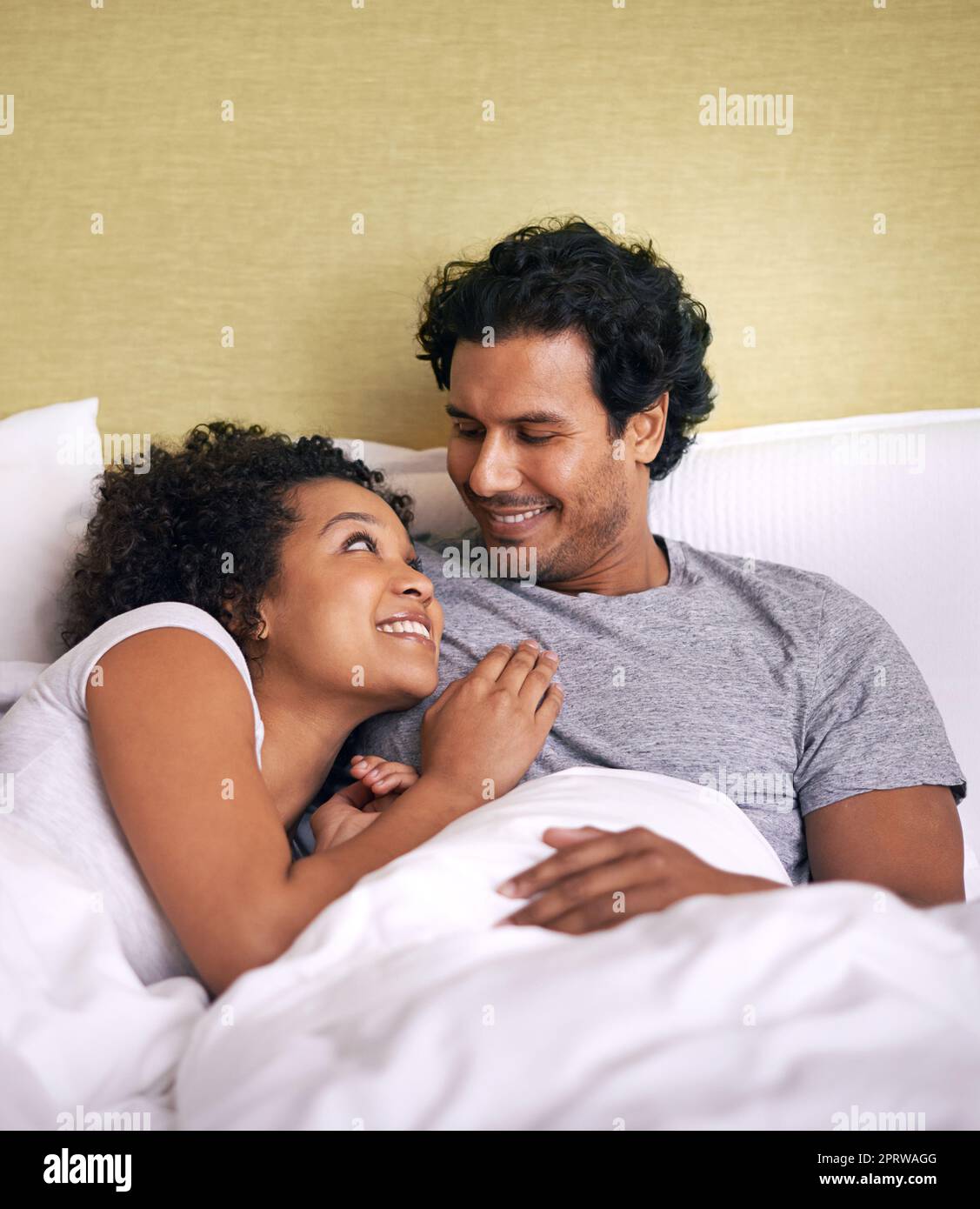 Cuddling with my hubby. A young husband and wife lying bed together. Stock Photo