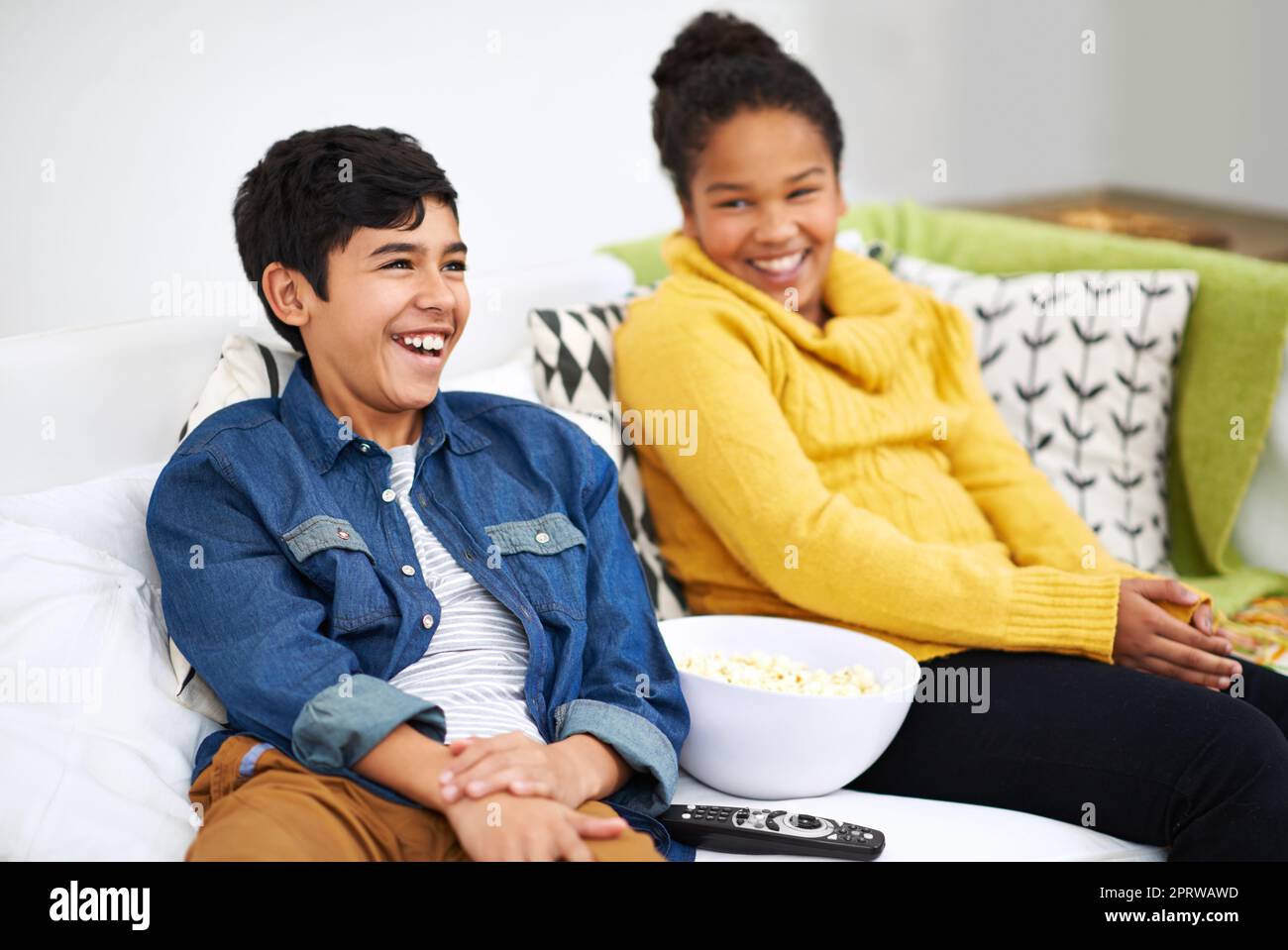 This is one funny flick. ethnic siblings holding a bowl of popcorn. Stock Photo