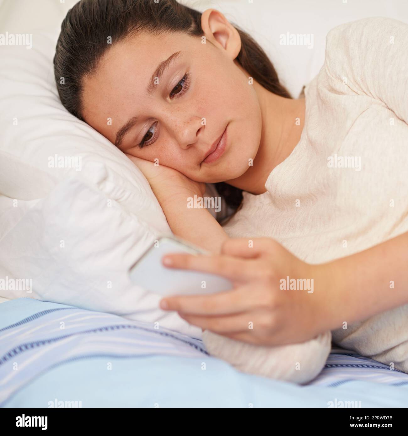 Cant put it down. a teenage girl lying on her bed and texting on her