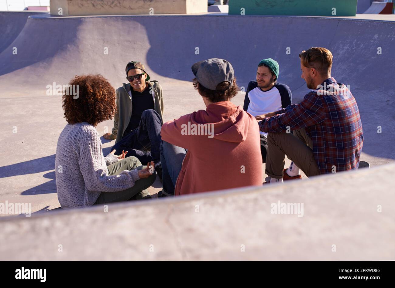 Chilling in the bowl. a group of friends hanging out in the sun at a skate park. Stock Photo