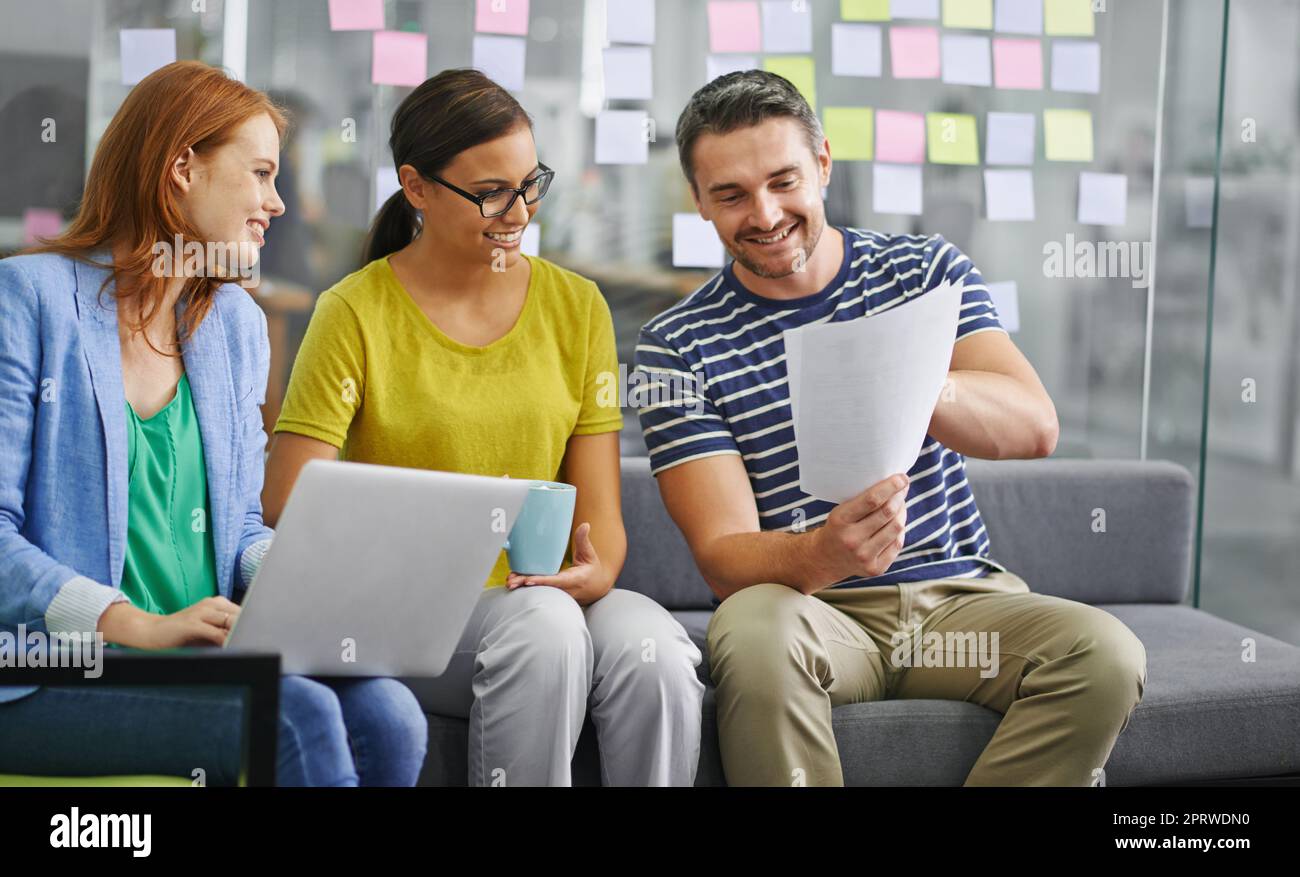 Weve got some great ideas going on here. Three coworkers smiling while looking over some paperwork in the office. Stock Photo