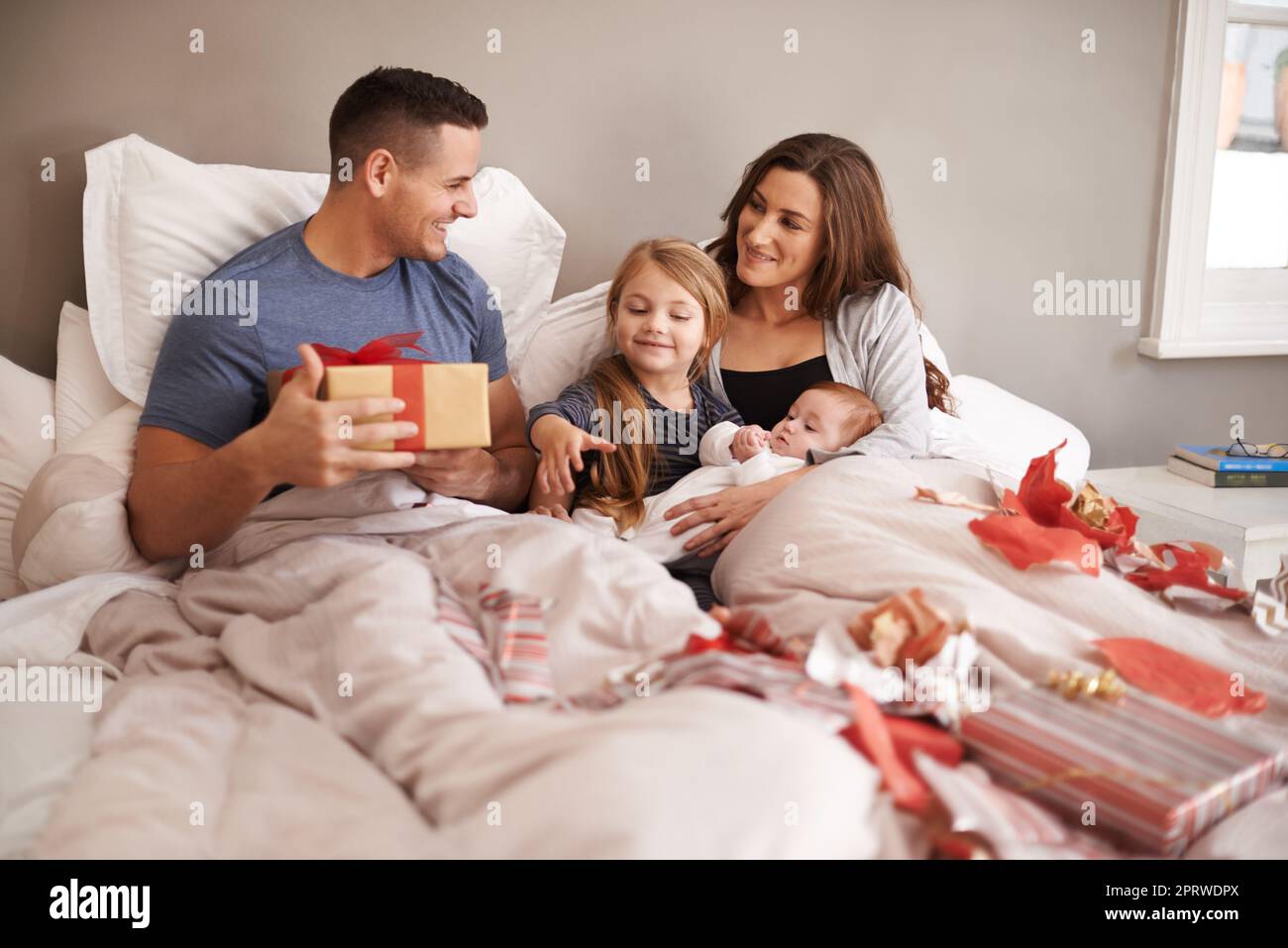 Is this one for me. an affectionate young family lying in bed and exchanging gifts. Stock Photo